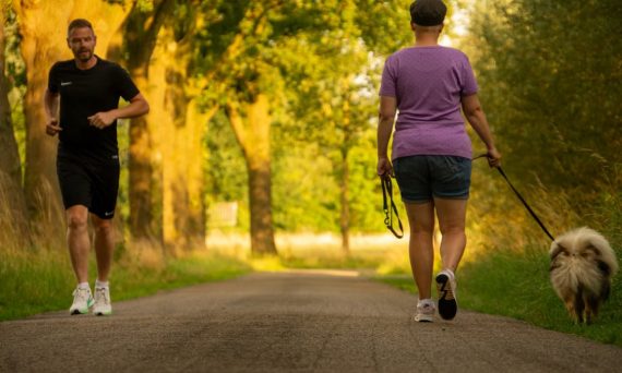 Man jogging and woman walking a dog on a picturesque outdoor path.